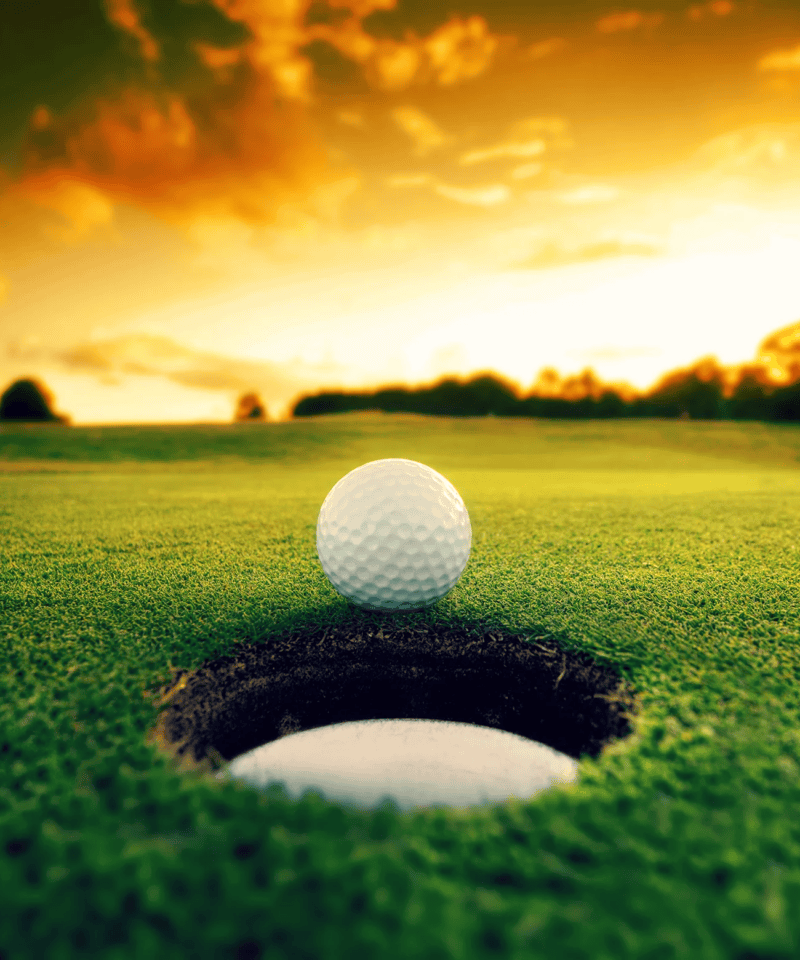 Golf ball resting at the edge of the hole on a green fairway at sunset